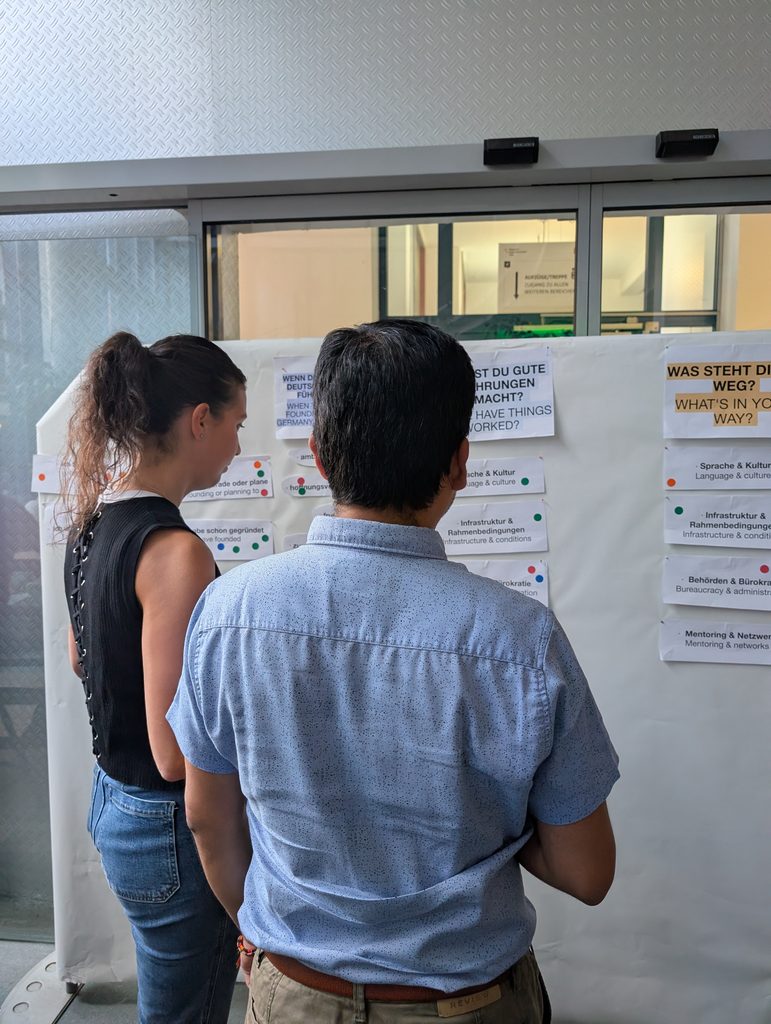 Hier sieht man zwei Workshopteilnehmende die vor der Wand stehen um die Fragen mit Punkten zu bekleben.